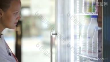 妇女打开冰箱，在透过冰箱门的商店视图选择牛奶